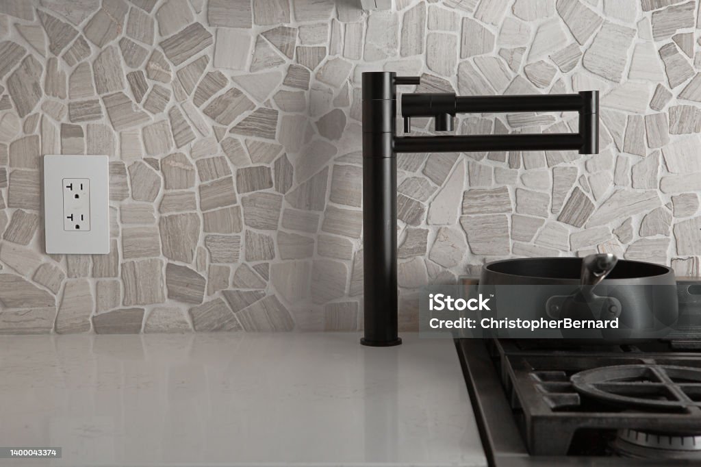 Schwarzer Topffüllerhahn über einem 6-Flammen-Gasherd in einer modernen Küche mit Steinrückwand.